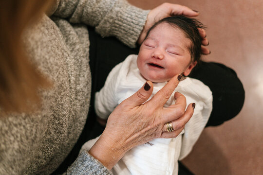 Cute smiling baby on laps of faceless senior woman