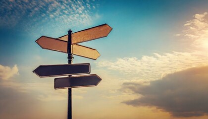 Blank directional road signs against blue sky. Black metal arrows on the signpost. Warm toned colors. Old style image
