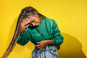Joyful black woman laughing with hand on head against yellow wall