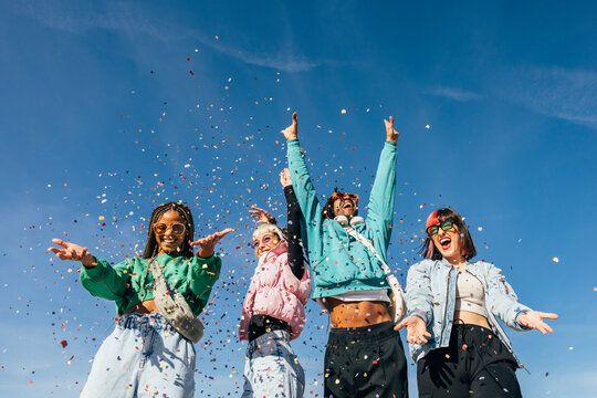 Joyful diverse friends celebrating with confetti under blue sky