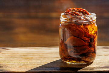 Sun dried tomatoes with herbs and sea salt in olive oil in a glass jar on wooden background, copy space.