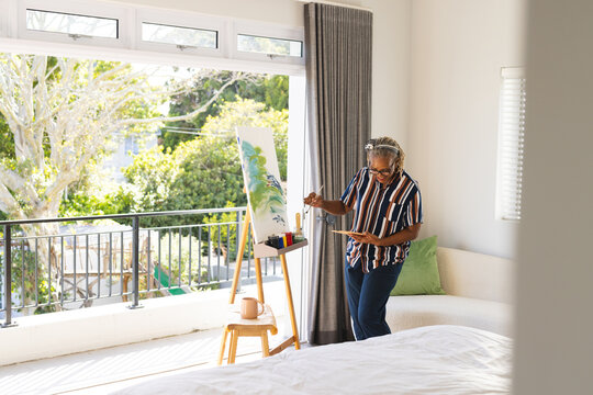 African American senior woman painting on canvas at home in sunny room, copy space