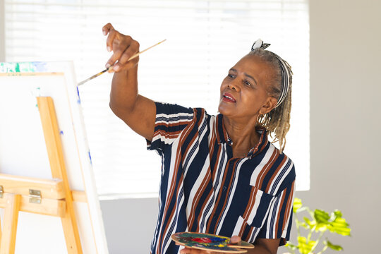 A senior African American woman is painting on canvas at home, copy space