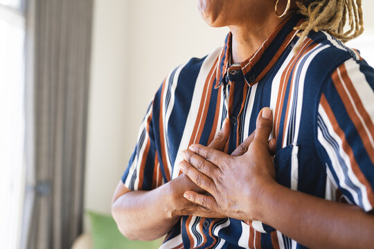 A senior African American woman with hands on her chest stands indoors at home, copy space