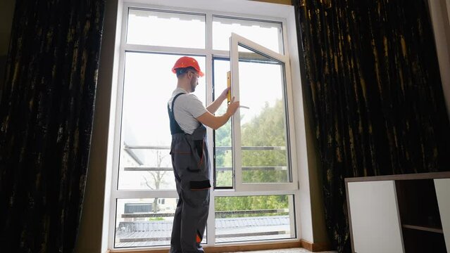 Window installer adjusting plastic windows with level tool in room
