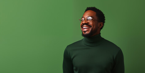 Fototapeta premium A man's bright smile and stylish eyewear radiate positivity, complemented by his sleek green turtleneck, against a matching deep green background.