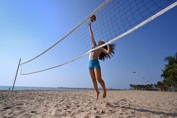 sportswoman jump to hit the ball in front of the net in the beach volleyball game