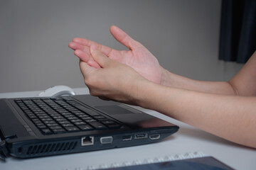 Young woman working in an office with carpal tunnel syndrome or wrist joint inflammation, massage...