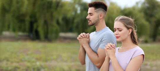 Young couple praying to God outdoors