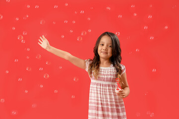 Cute little girl blowing soap bubbles on red background