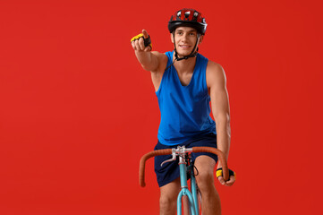 Young man riding bicycle and pointing at something on red background