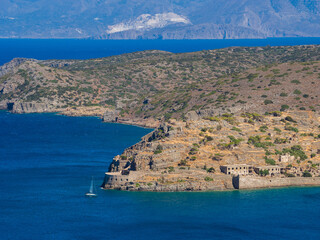 Spinalonga island with a yacht and peninsula behind (Plaka, Crete, Greece) - obrazy, fototapety, plakaty