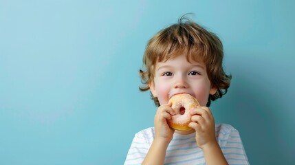 Cute little boy eating a donut on a blue background - obrazy, fototapety, plakaty