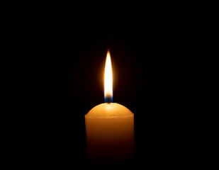 A single burning candle flame or light glowing on a big yellow candle on black or dark background...