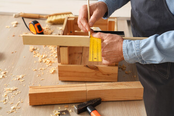 Mature carpenter measuring wooden box at table in workshop, closeup