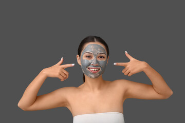 Young woman with clay mask on her face against grey background