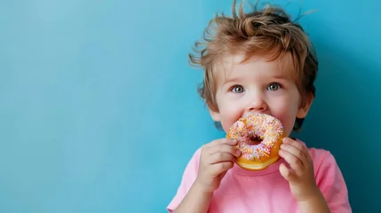 Foto op Plexiglas The child eats a donut on a blue background © Sittipol 