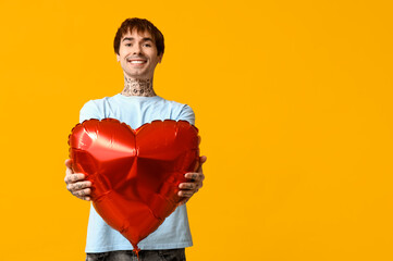 Handsome young man with heart-shaped air balloon on yellow background