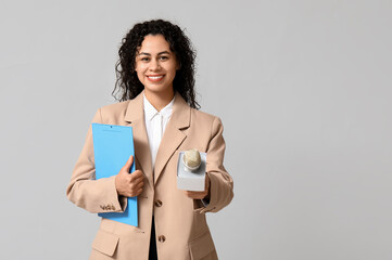 Beautiful young happy African-American female journalist with microphone and clipboard on grey...