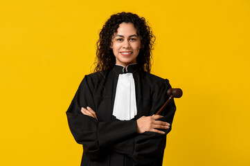 Beautiful young happy African-American female judge with gavel on yellow background