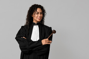 Beautiful young happy African-American female judge with gavel on grey background - obrazy, fototapety, plakaty