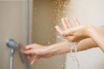 A woman uses hand to measure the water temperature from a water heater before taking a shower.