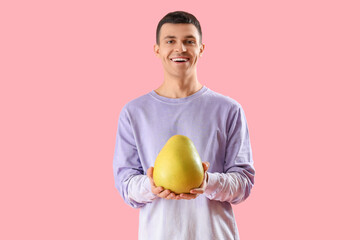 Young man with pomelo on pink background