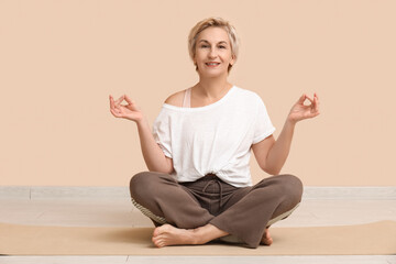Portrait of meditating mature woman sitting on floor against beige wall