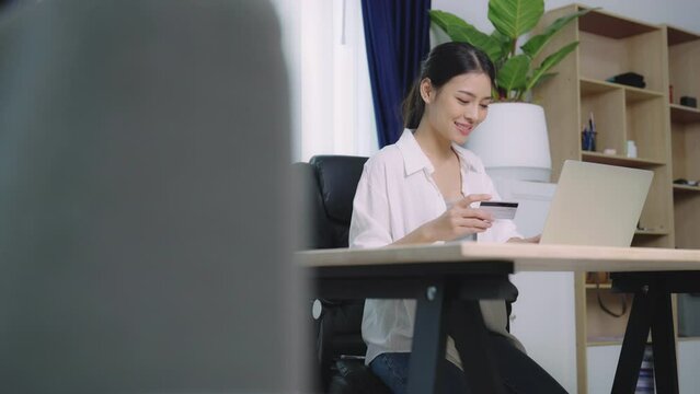 Young asian woman makes online banking payments through the internet from bank card on computer laptop. Shopping online on notebook with credit card