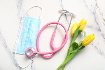 Stethoscope with mask and yellow tulips for International Nurses Day on white grunge background