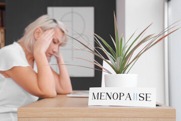Paper with word MENOPAUSE and plant on table of mature businesswoman in office, closeup