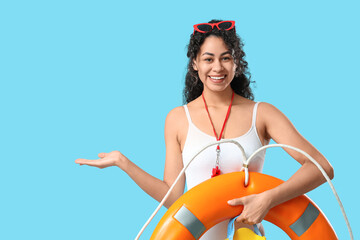 Beautiful young happy African-American female lifeguard with ring buoy and flippers pointing at...
