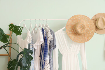 Rack of trendy clothes and hats near white wall