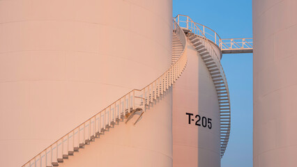 Curve lines pattern of spiral staircase on group of white storage fuel tanks with orange sunlight...