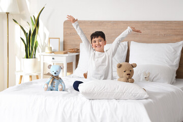Cute happy little boy with toys sitting in bedroom