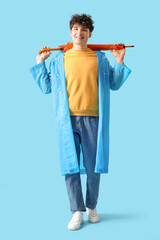 Young man in raincoat with umbrella on blue background