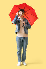 Young man in headphones with umbrella listening to music on yellow background
