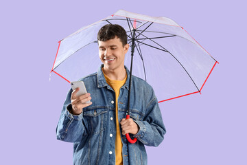 Young man with transparent umbrella using mobile phone on lilac background