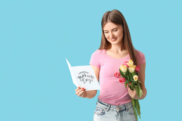Happy young woman with bouquet of tulips and greeting card with text HAPPY MOTHERS DAY on blue background