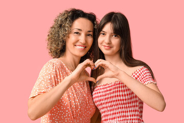 Beautiful mature woman with her teenage daughter showing heart gesture on pink background. Mother's...