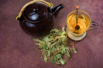 glass cup with teapot and fresh linden leaves, infusion of lime blossom tea, medicinal plant with...