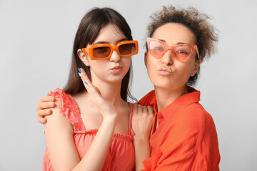 Beautiful mature woman with her teenage daughter in sunglasses on grey background. Mother's day