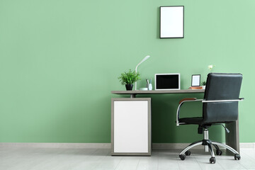 Stylish workplace with modern laptop, books, lamp and stationery near green wall in office