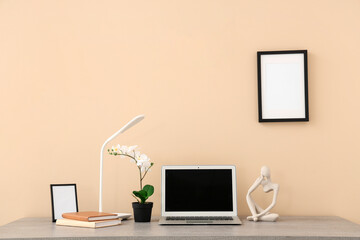 Stylish workplace with modern laptop, books, decor and lamp near beige wall in office