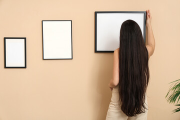 Young woman hanging picture frame on beige wall in room