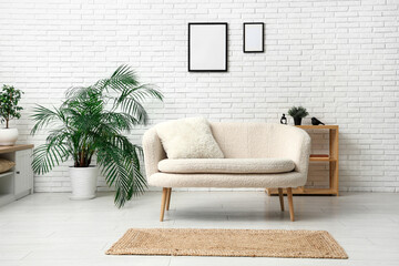 Modern living room with houseplant, sofa and blank picture frame on white brick wall