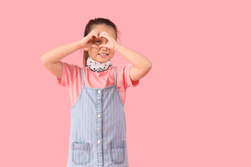 Portrait of fashionable little girl making heart gesture on pink background