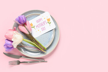 Table setting with greeting card for Mother's day and tulips on pink background