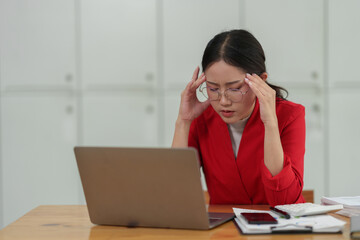 Young independent businesswoman with glasses is tired, stressed, has a headache while sitting in front of a laptop for a long time and working in finance. Online. Office Syndrome concept.