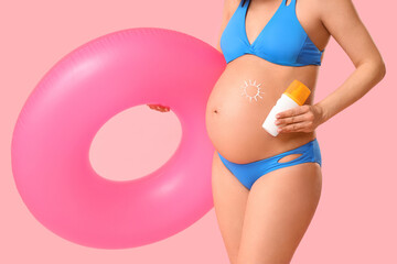 Young pregnant woman with inflatable ring and sunscreen on pink background. Travel concept